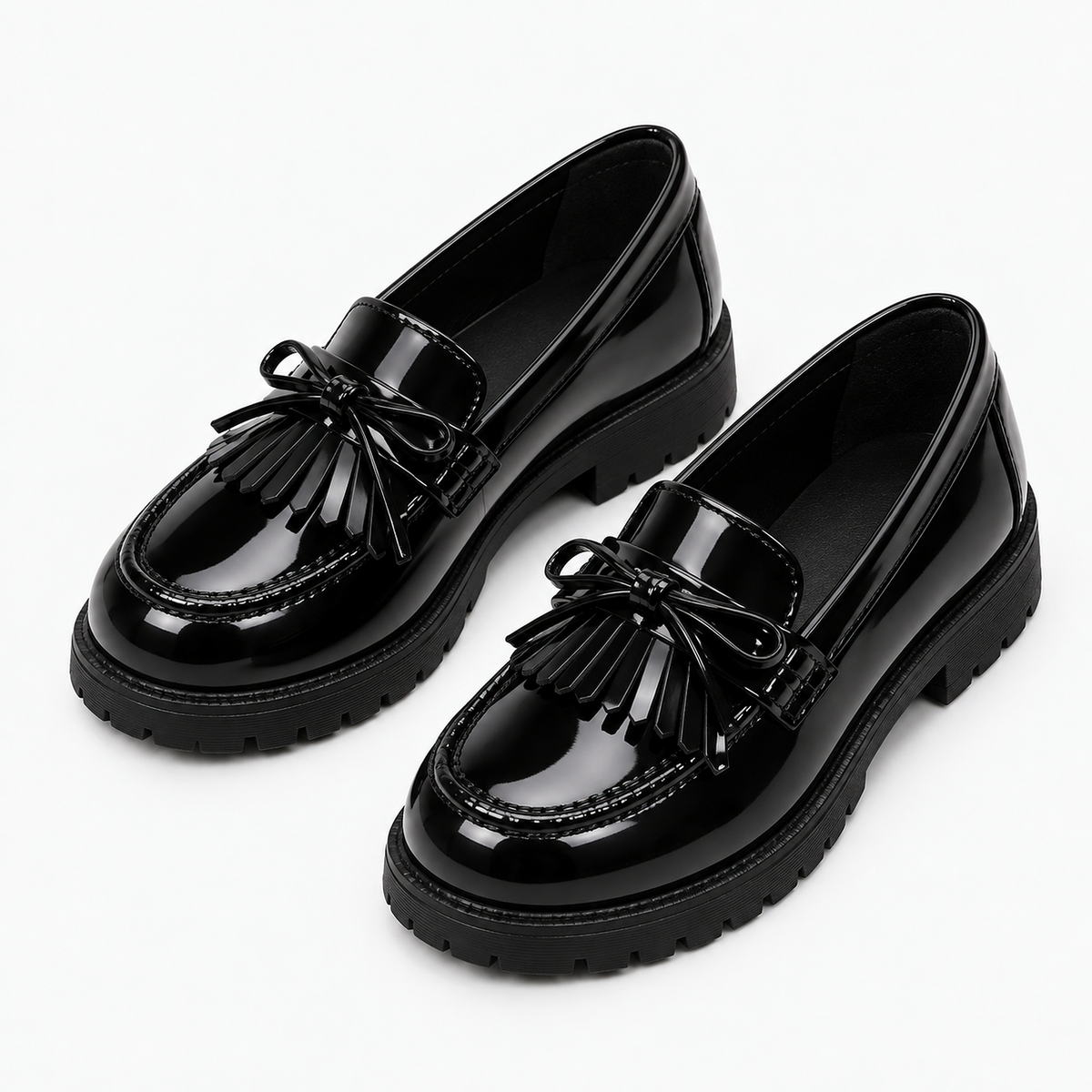 Kids Tassel Bow Loafers Black - angled pair product photo. Premium angled pair studio photo of black glossy kids tassel bow loafers with neat tassel bow detail and chunky black lug soles.