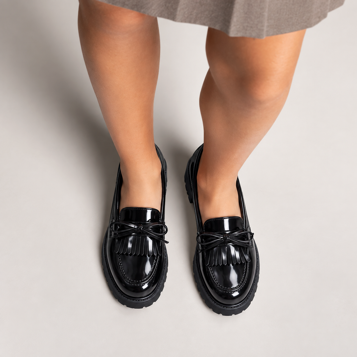 Kids Tassel Bow Loafers Black - worn styling view. Elegant worn product photo of black glossy kids tassel bow loafers, styled on feet with neat bow detail and premium studio lighting.